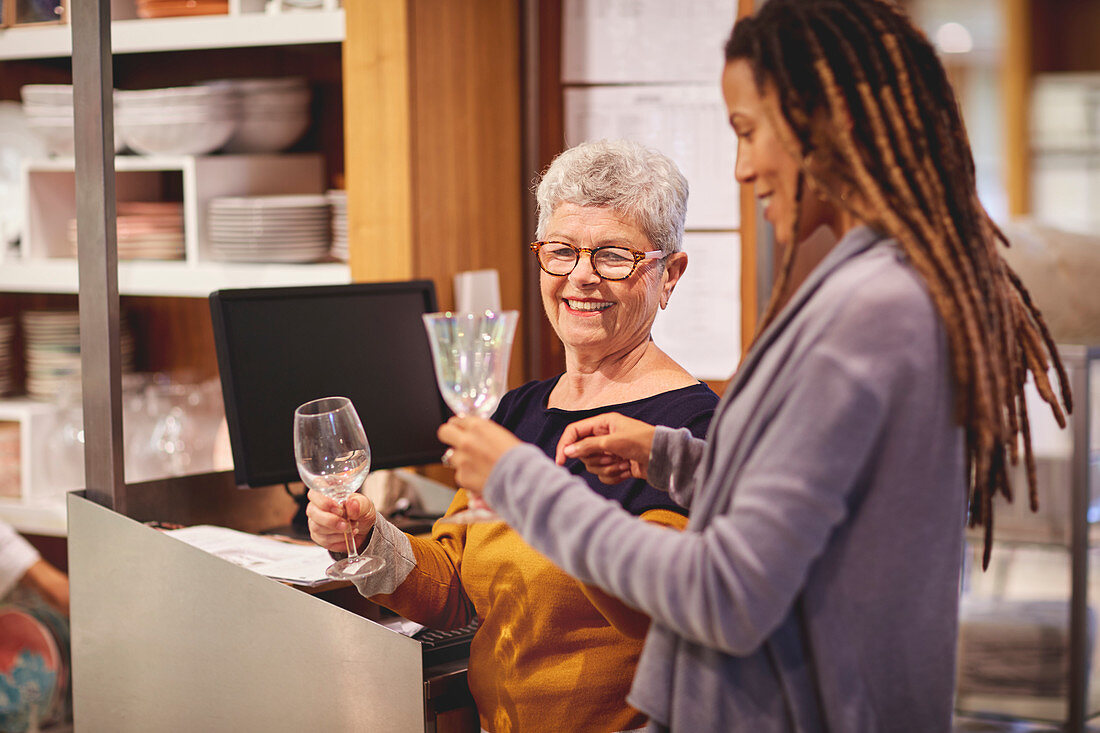 Smiling worker helping woman shopping for wine glasses