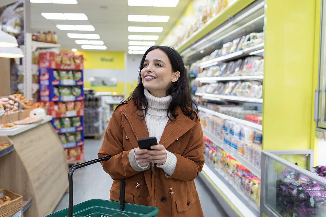 Woman with smart phone grocery shopping in supermarket
