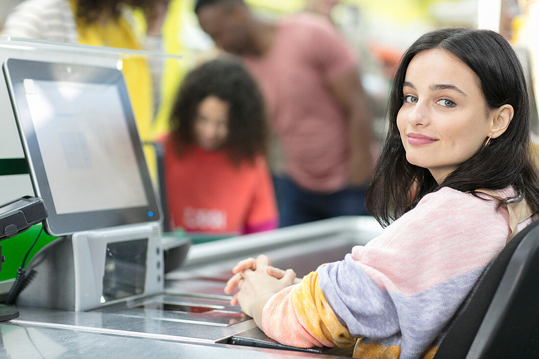 Young female cashier working at checkout in supermarket