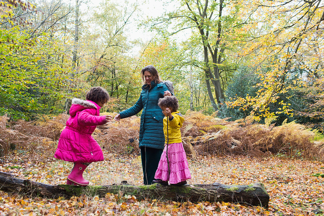 Mother and daughters playing on fallen log in autumn woods