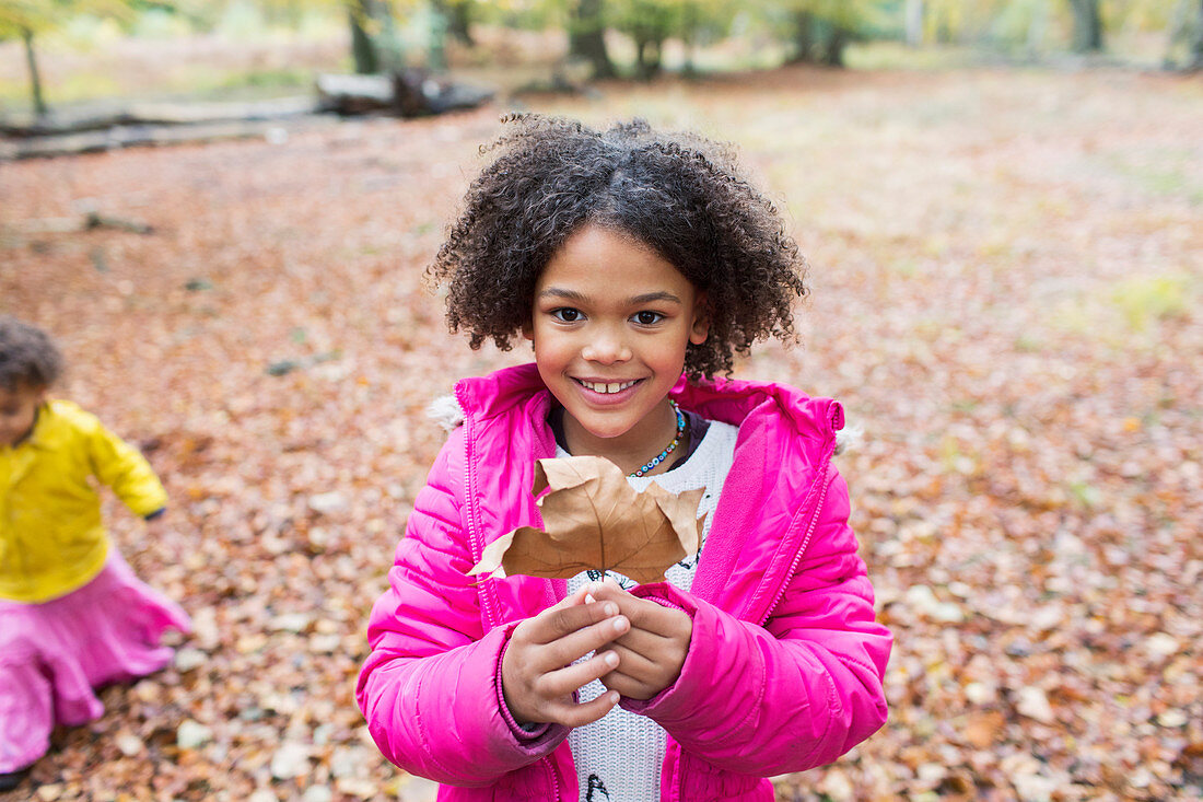 Portrait happy girl holding autumn leaf in woods