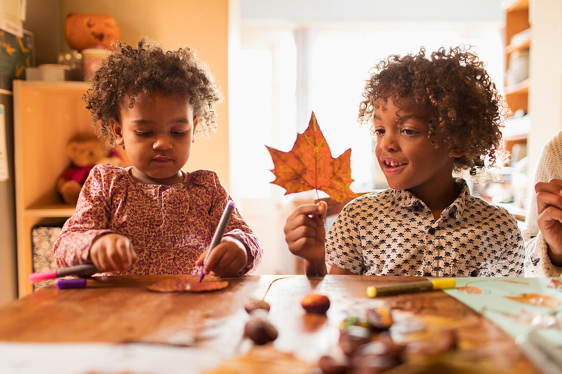 Brother and sister making crafts with autumn leaf at table