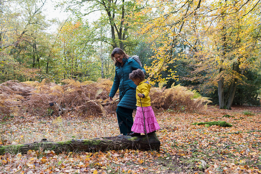 Mother and daughter walking on fallen log in autumn woods