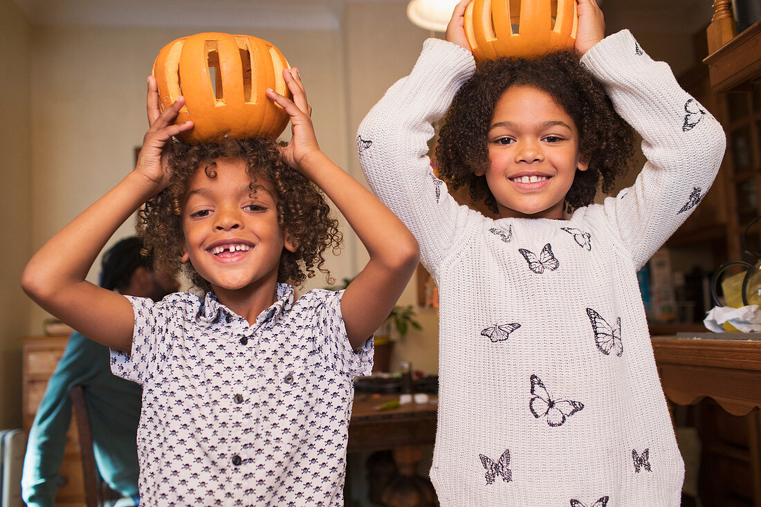 Happy brother and sister holding carved pumpkins overhead