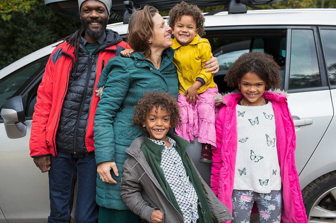 Portrait happy multiethnic family standing outside car