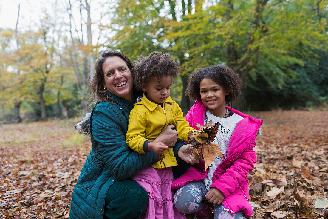 Mother and daughters playing in autumn leaves in woods