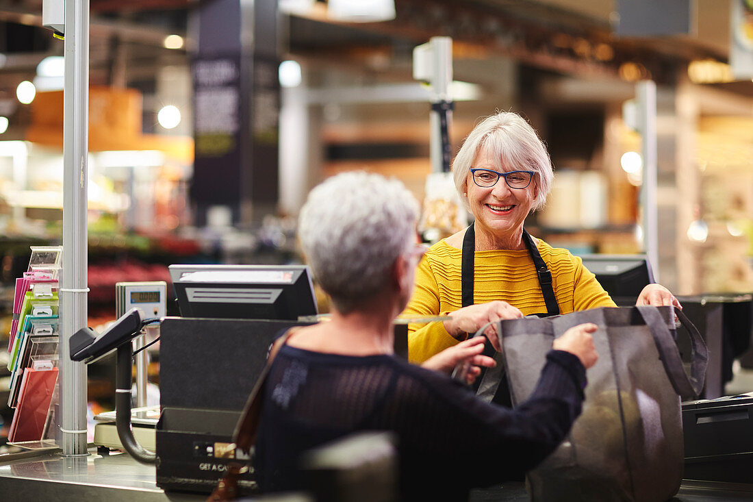 Senior female cashier helping customer supermarket checkout