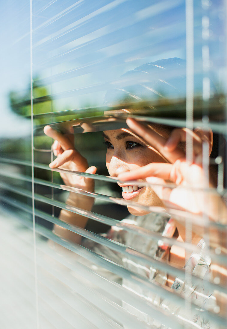 Smiling woman peering out window blinds