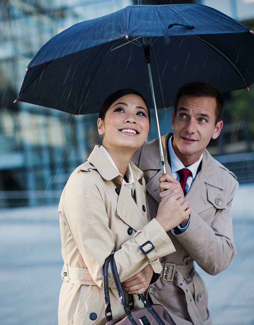 Businessman and businesswoman watching rain under umbrella