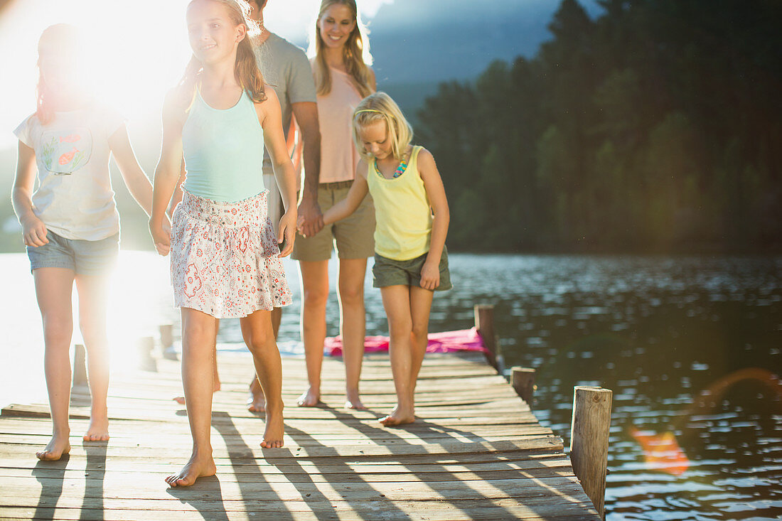 Family holding hands and walking on dock over lake