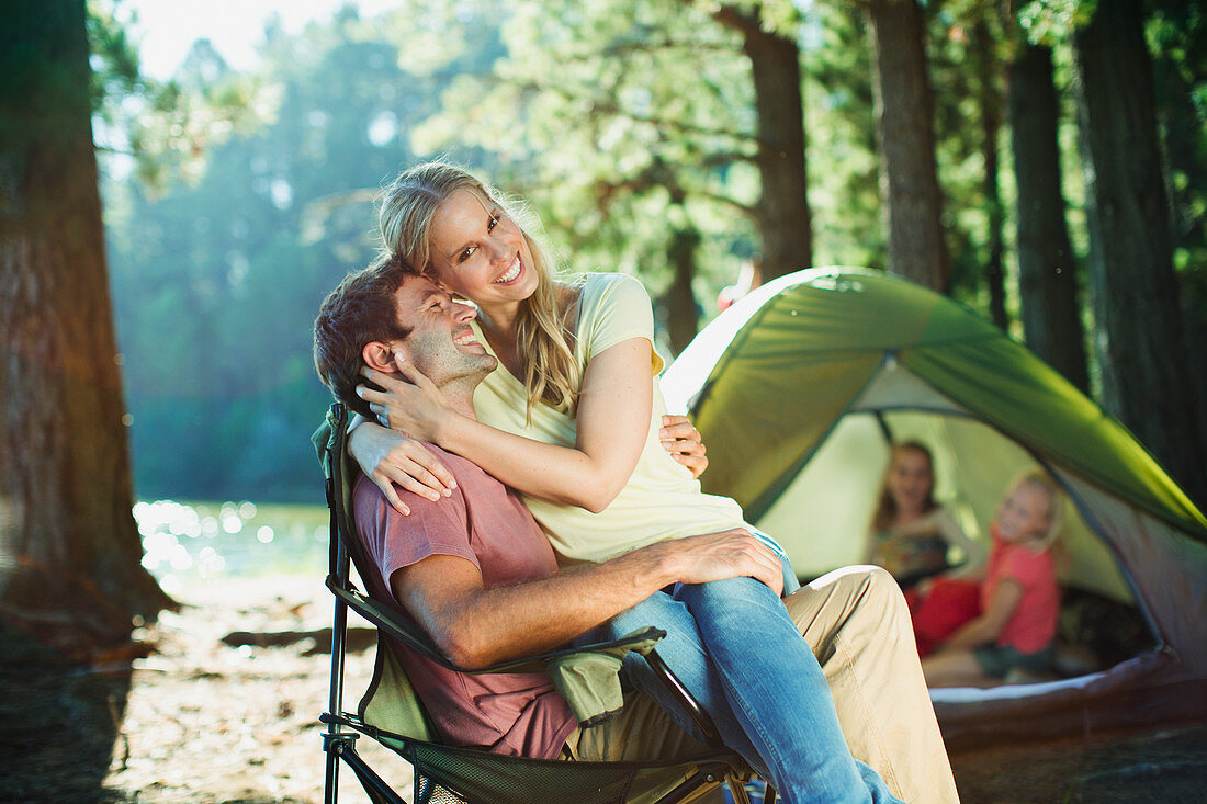 Smiling woman sitting on husbands lap at campsite in woods