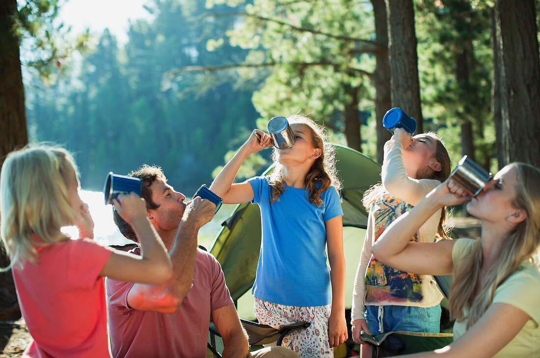 Family drinking from mugs at campsite in woods