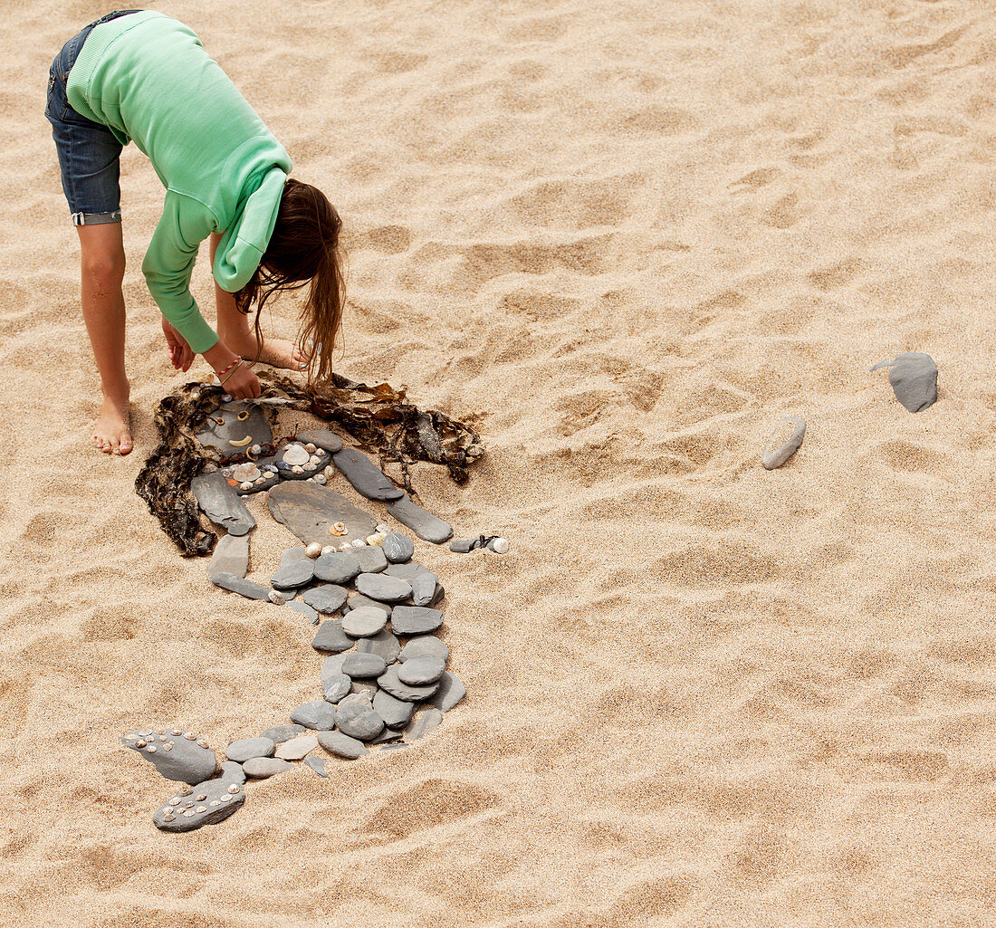 Girl making mermaid from rocks and seaweed on beach