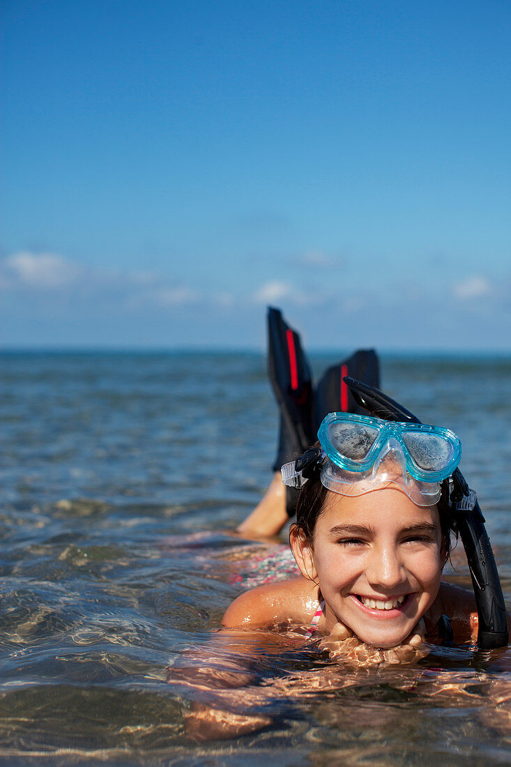 Smiling girl with snorkel and goggles laying in ocean