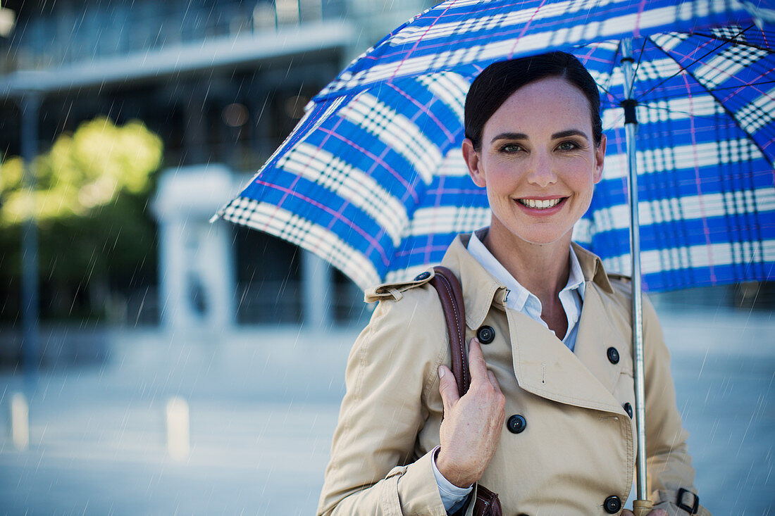 Smiling businesswoman in trench coat under umbrella