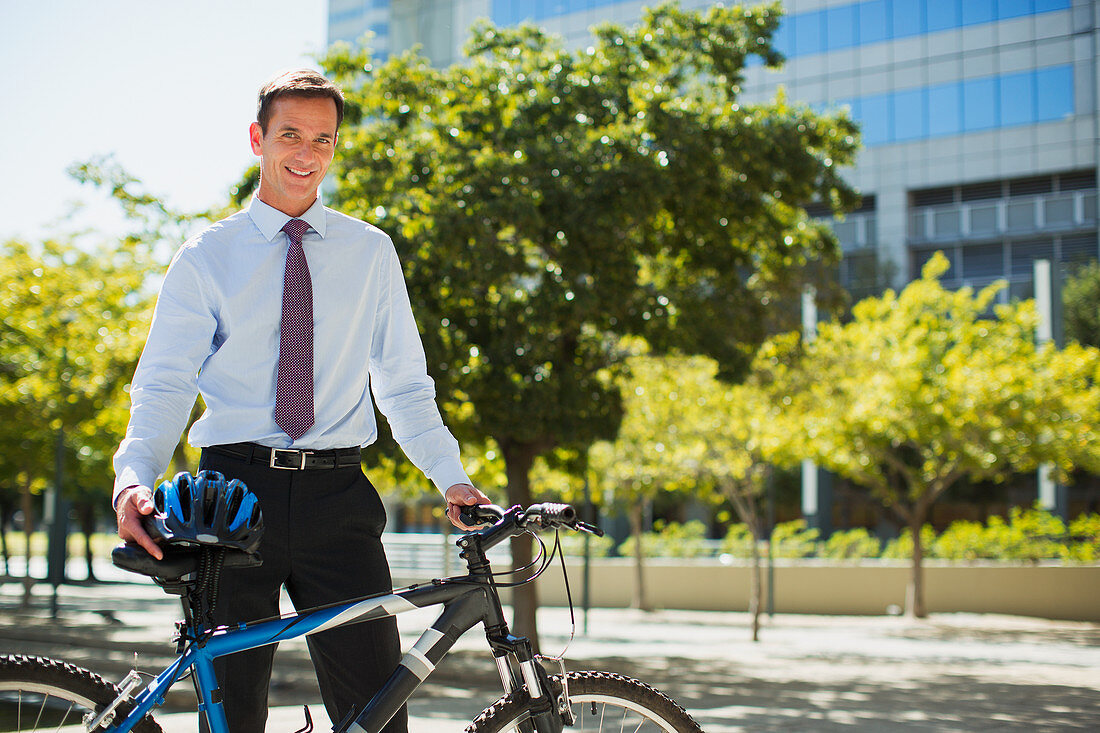 Smiling businessman with bicycle and helmet in urban park