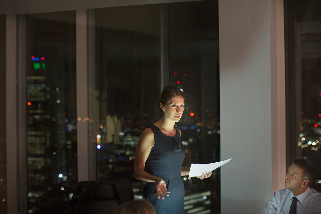 Businesswoman leading meeting in conference room at night
