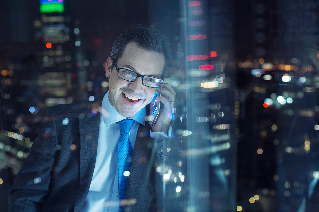 Businessman talking on cell phone in urban window at night
