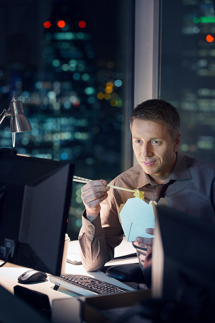 Businessman eating take out food at desk in office at night