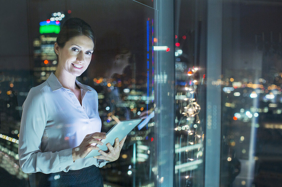 Businesswoman using digital tablet in urban window at night