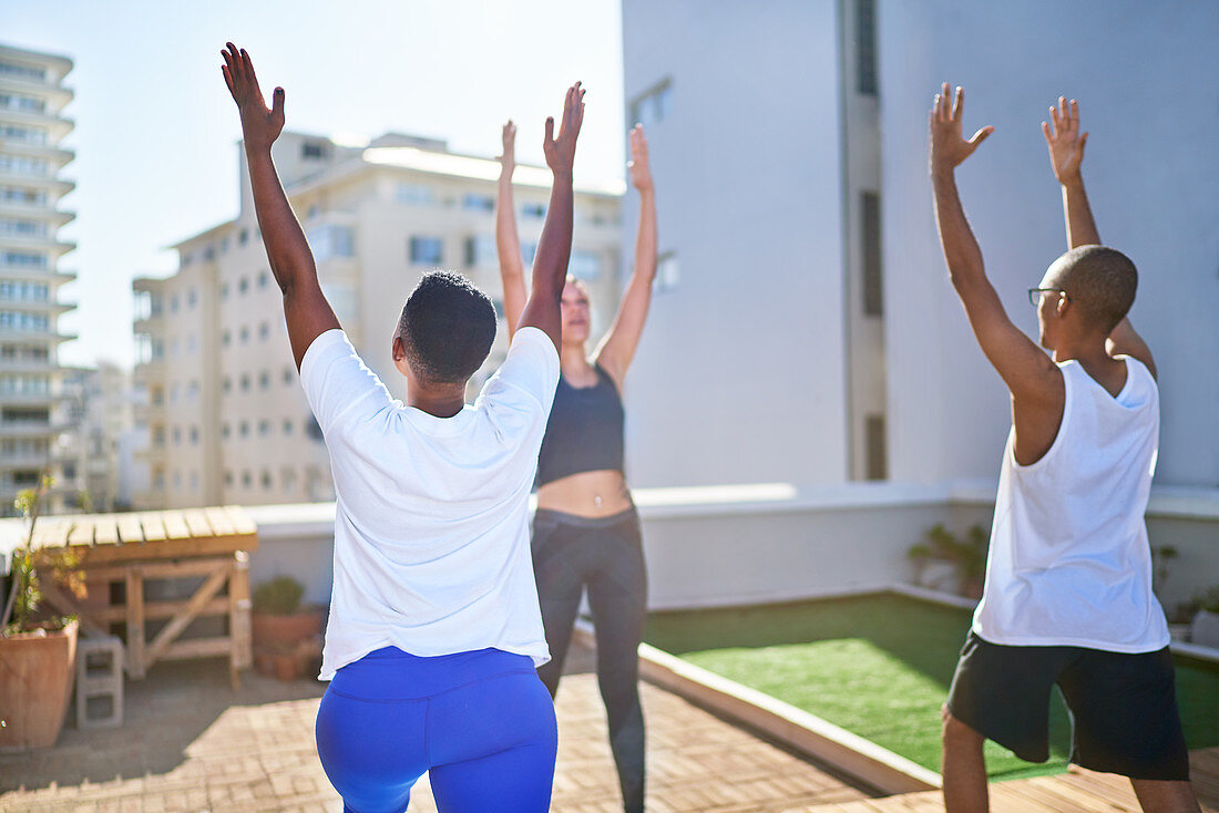 Friends practicing yoga on sunny urban rooftop