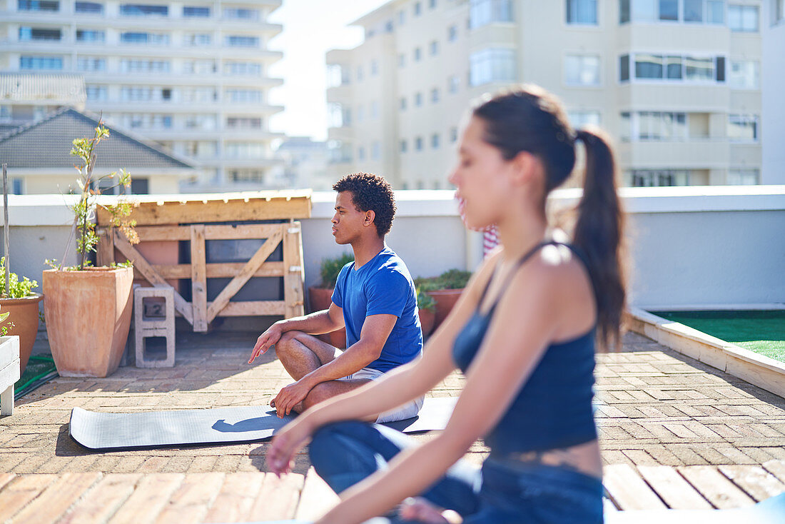 Young man and woman practicing yoga on sunny urban rooftop