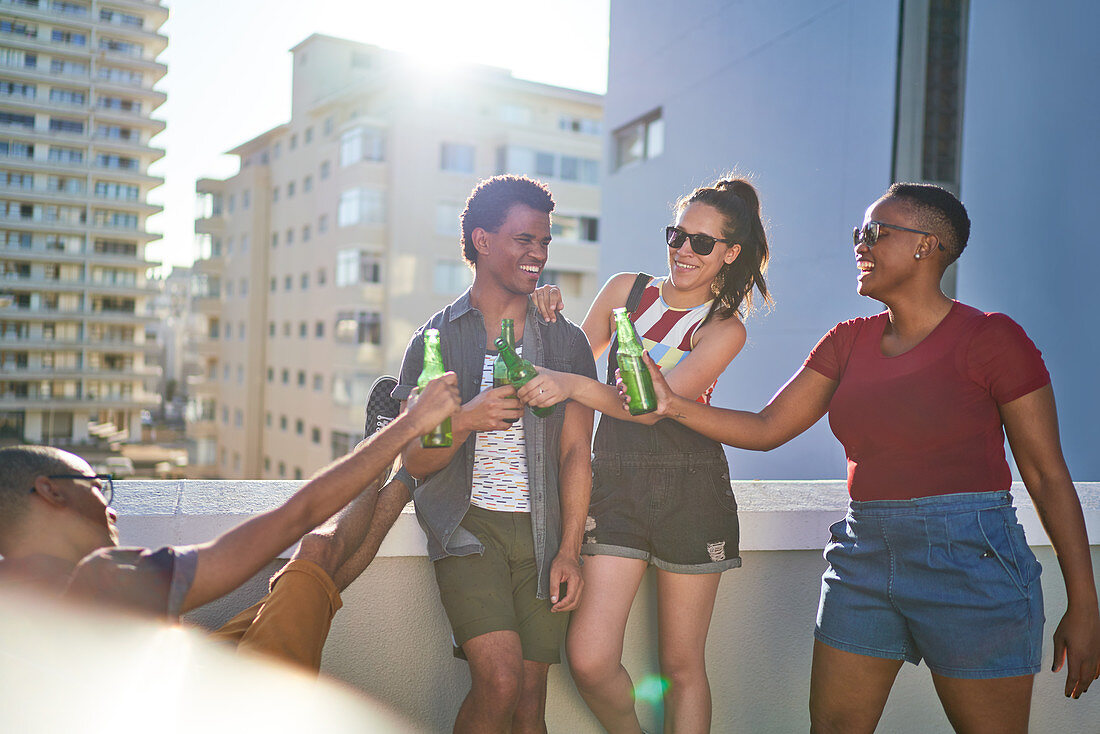 Happy young friends toasting beer bottles on sunny balcony