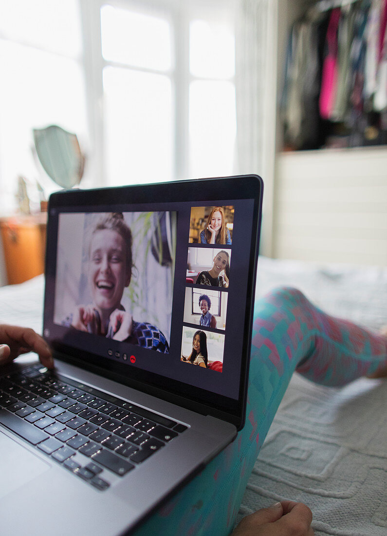 Woman with laptop video chatting with friends on bed