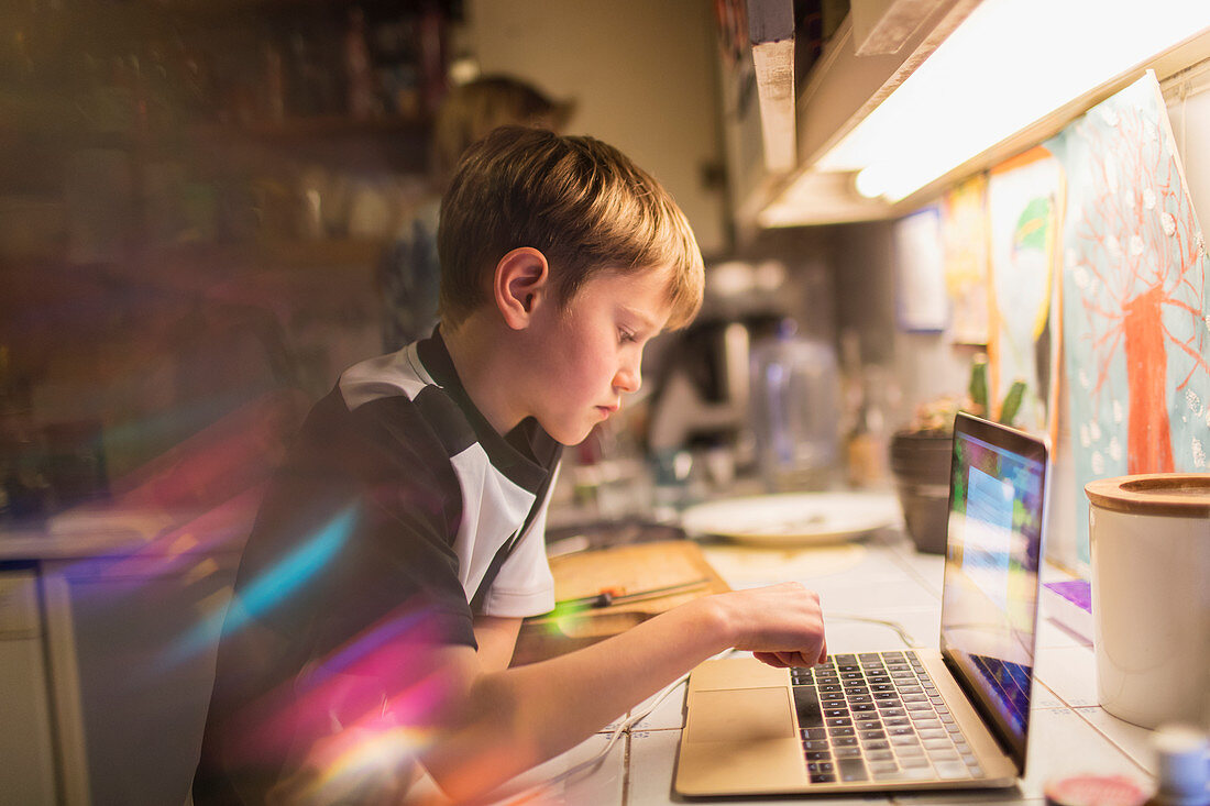 Focused boy doing homework at laptop in kitchen