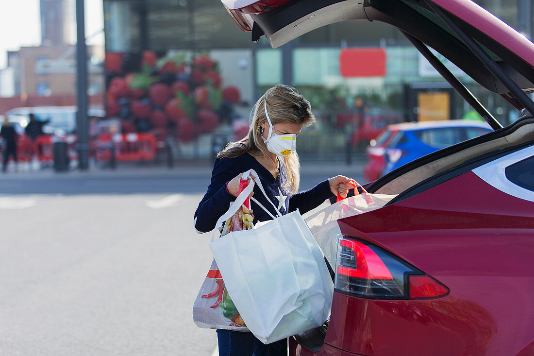 Woman with face mask loading groceries into car