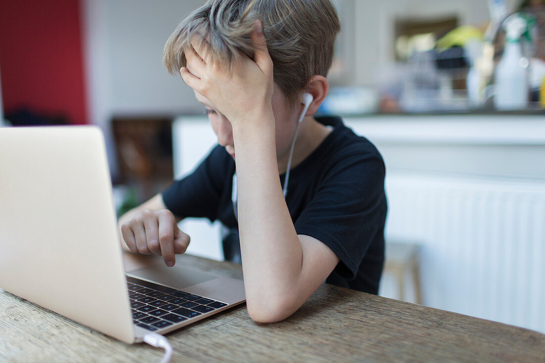Frustrated boy with headphones homeschooling at laptop
