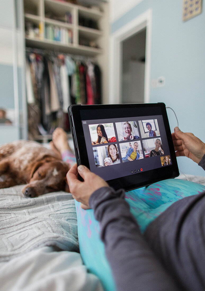 Woman video chatting with friends on bed with dog
