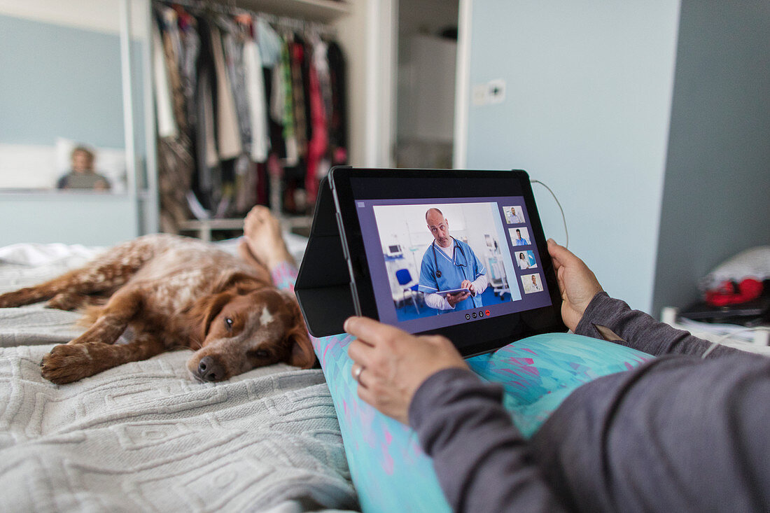 Woman with tablet video chatting with doctor on bed with dog