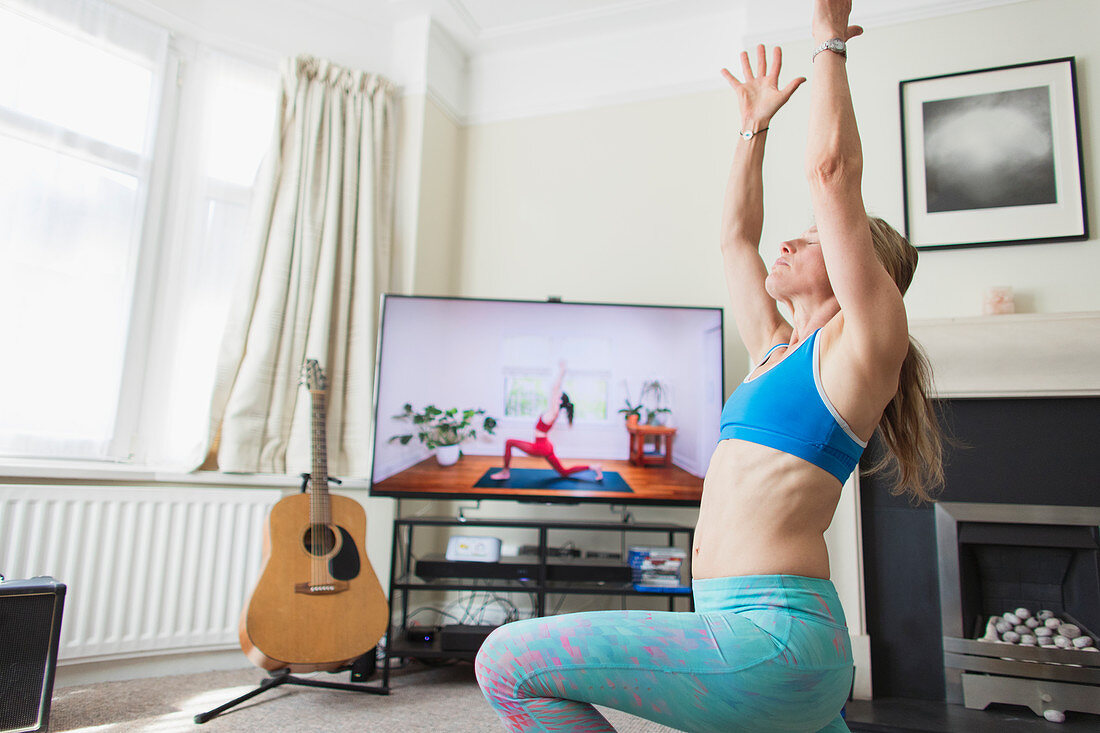 Woman practicing yoga at TV in living room