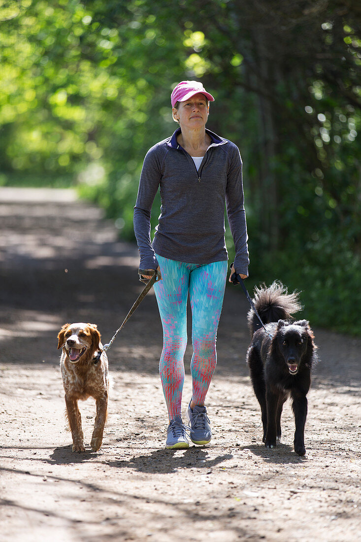 Woman with dogs walking on sunny trail