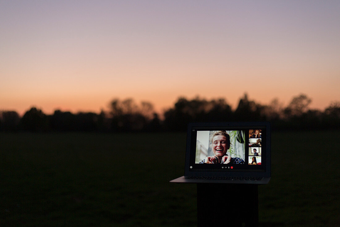 Friends video chatting on laptop screen in park at dusk