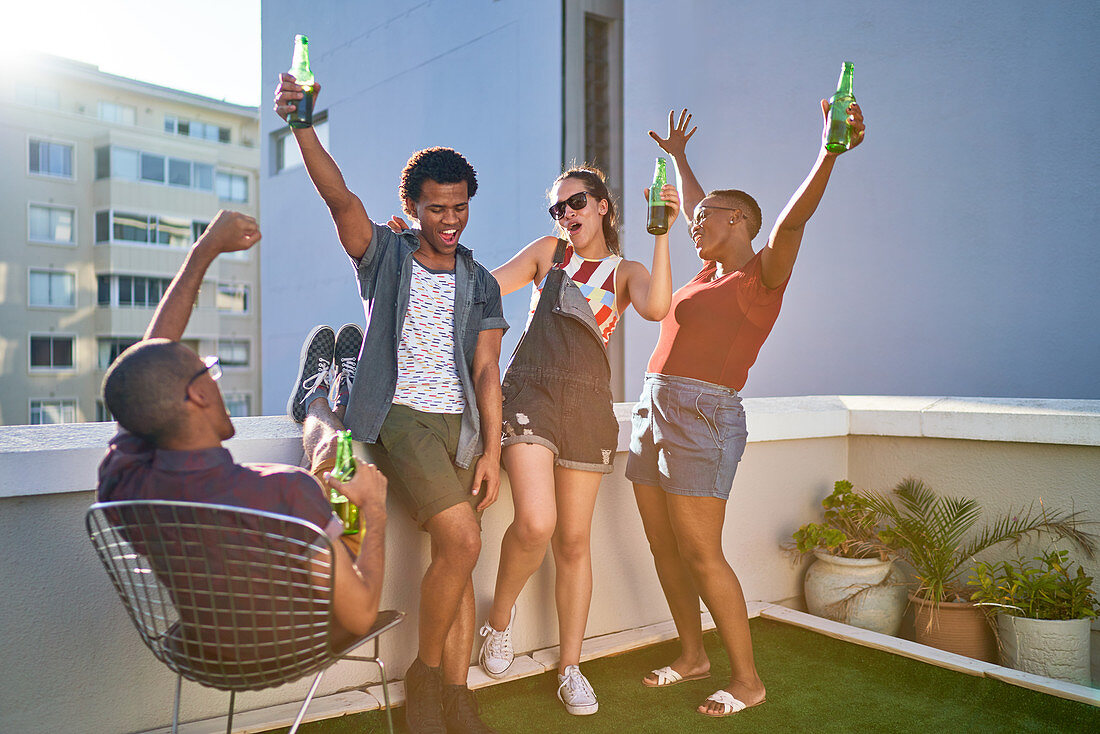 Young friends cheering and drinking beer on urban rooftop