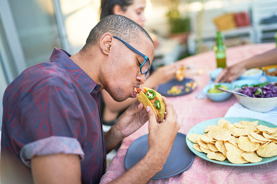 Young man eating taco at patio table