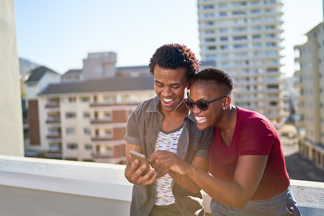 Happy young couple using smart phone on rooftop balcony