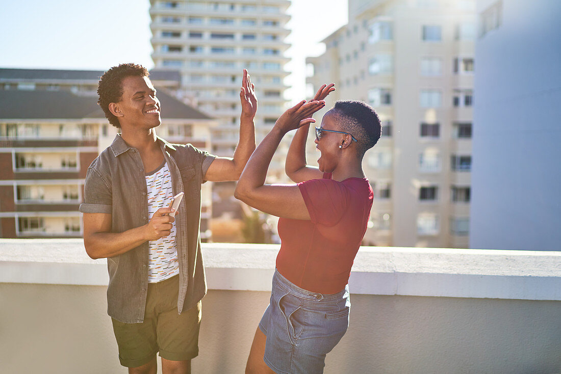 Happy young couple high fiving on sunny rooftop balcony