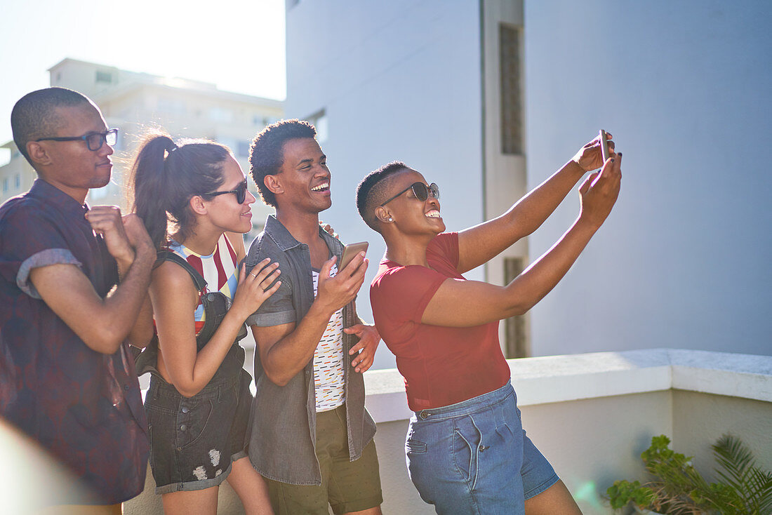 Happy young friends taking selfie on sunny urban balcony