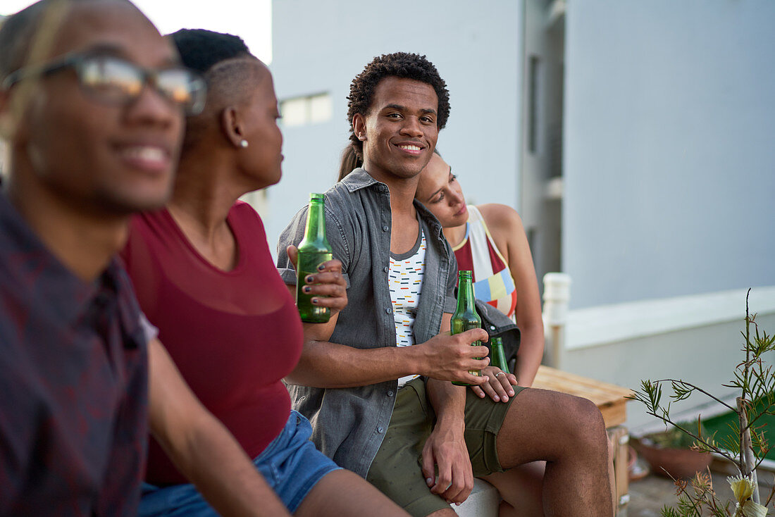 Confident young man drinking beer with friends on patio