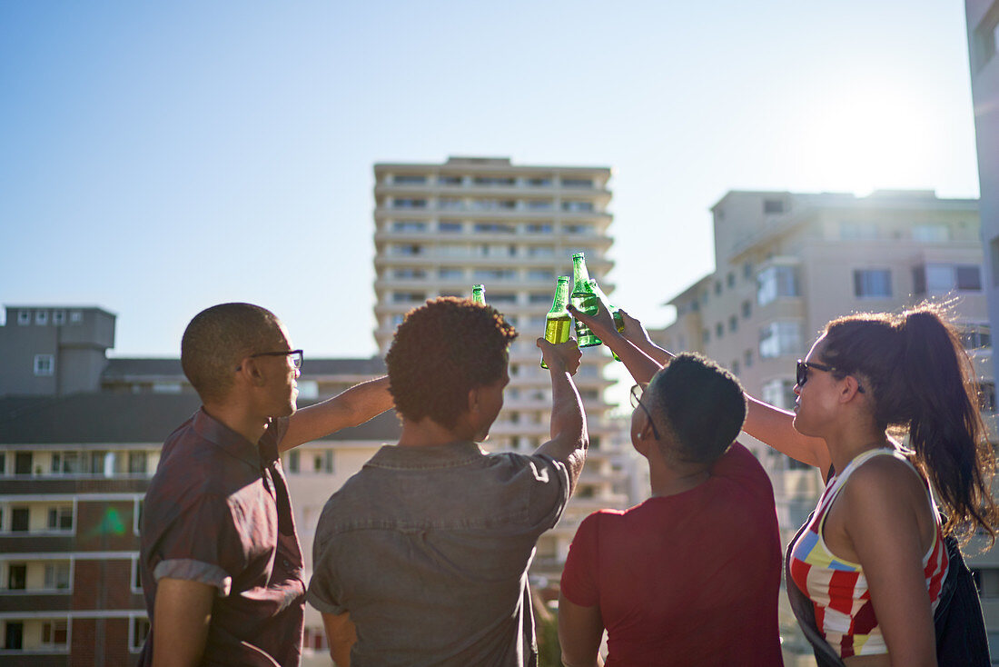 Young friends toasting beer bottles on rooftop balcony