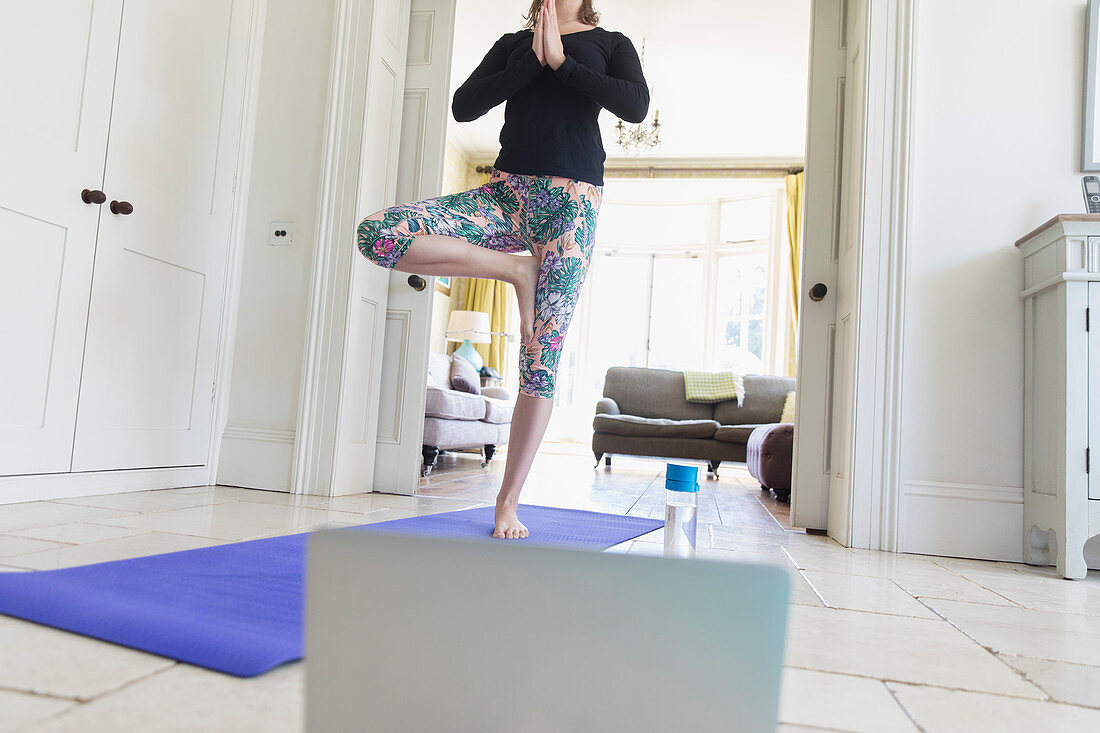 Woman practicing yoga online with laptop at home