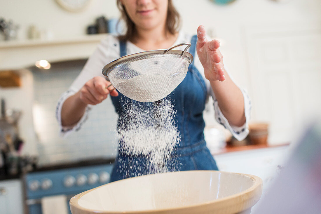 Teenage girl sifting flour in kitchen