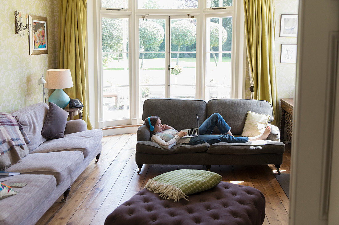 Teenage girl with headphones relaxing on living room sofa