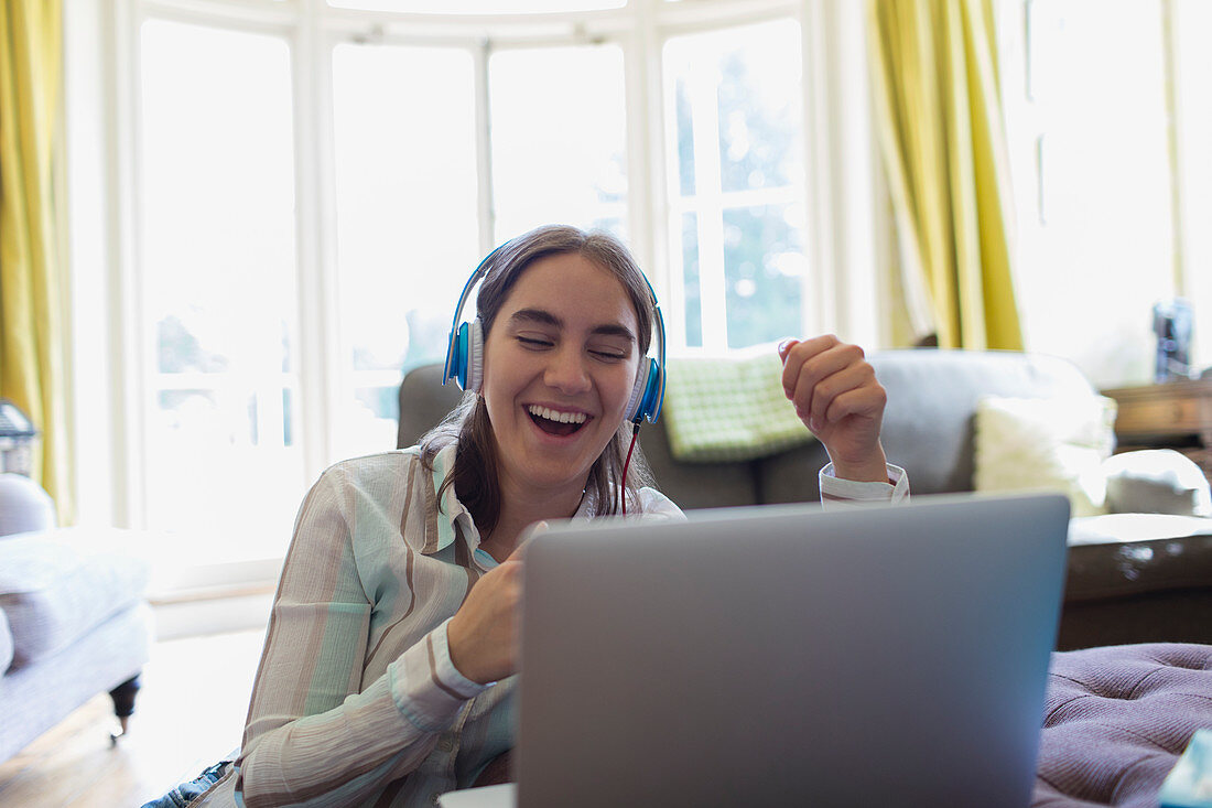 Happy teenage girl with headphones video chatting at laptop