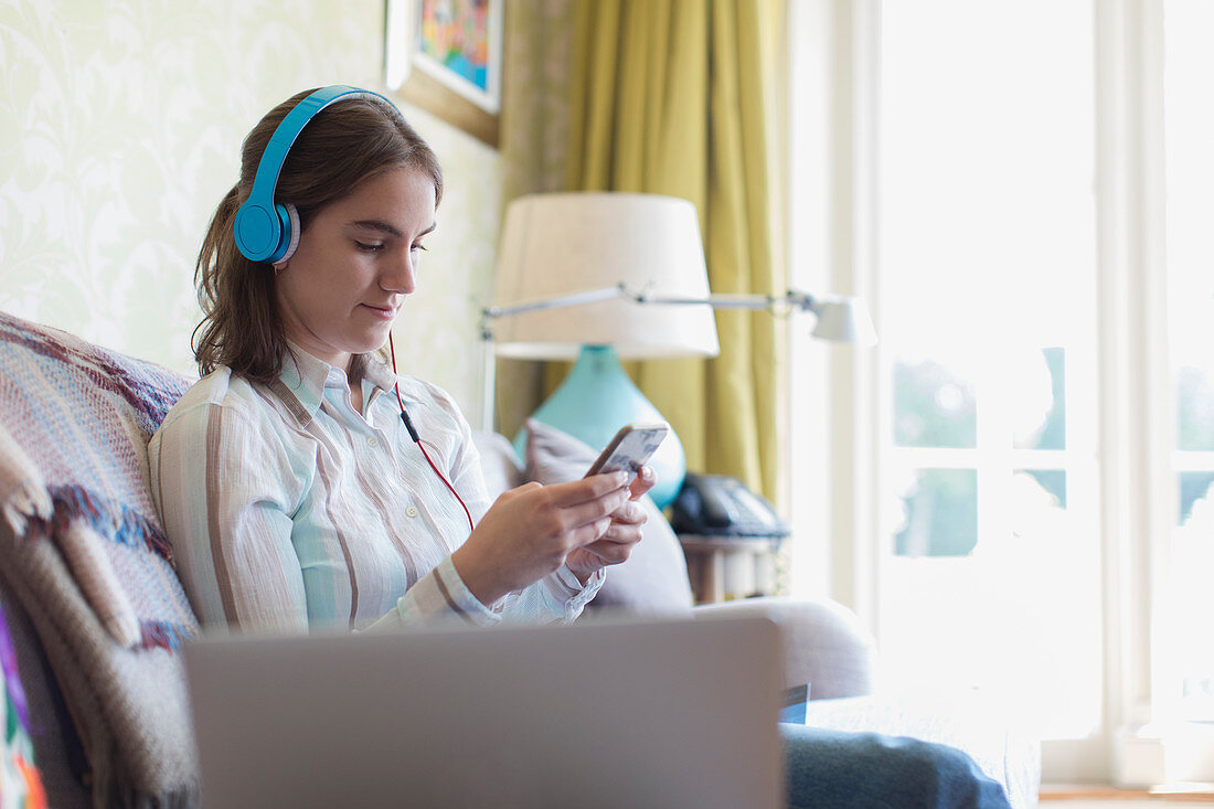 Teenage girl with headphones and smart phone on sofa