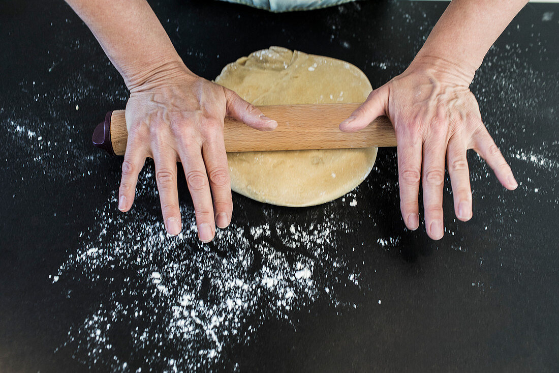 Woman rolling dough with rolling pin on floured counter