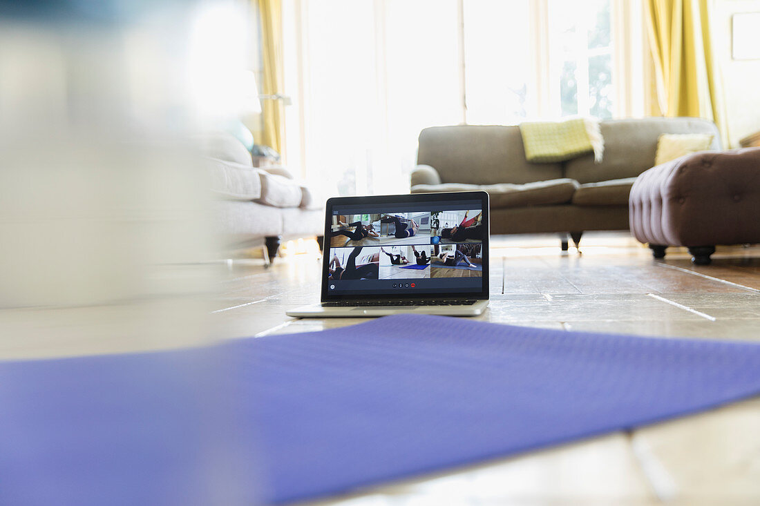 Exercise class streaming on laptop screen behind yoga mat